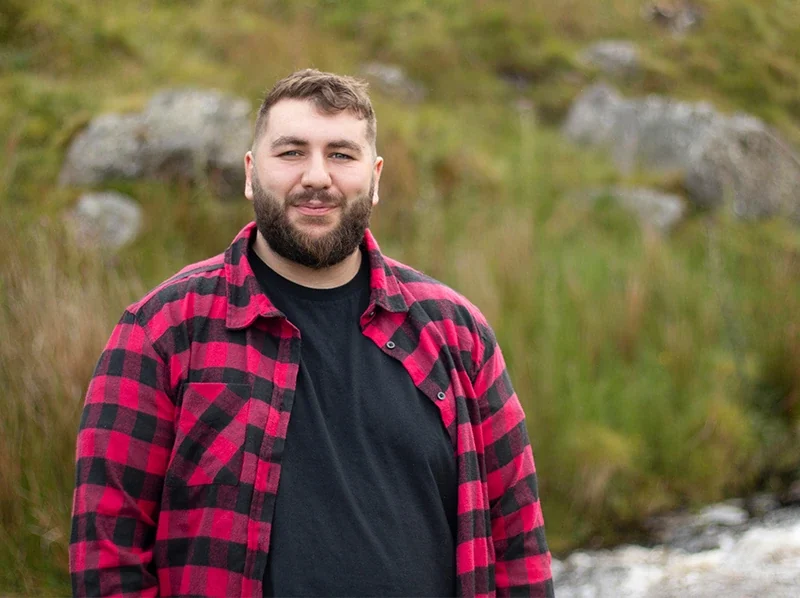 Overweight man in flannel standing outside with smile