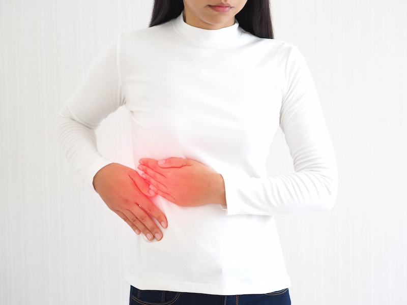 Woman in white touching her upper right side of abdomen