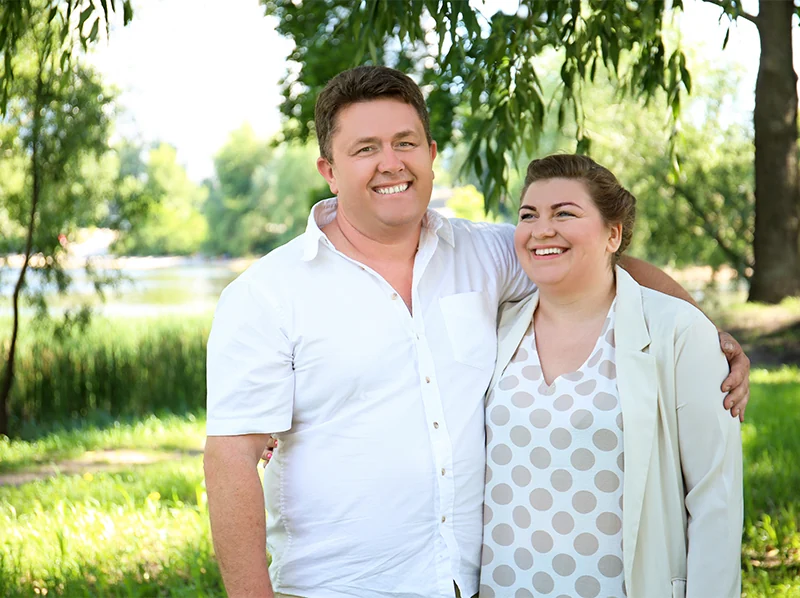 Overweight couple smiling with arms around each other in park