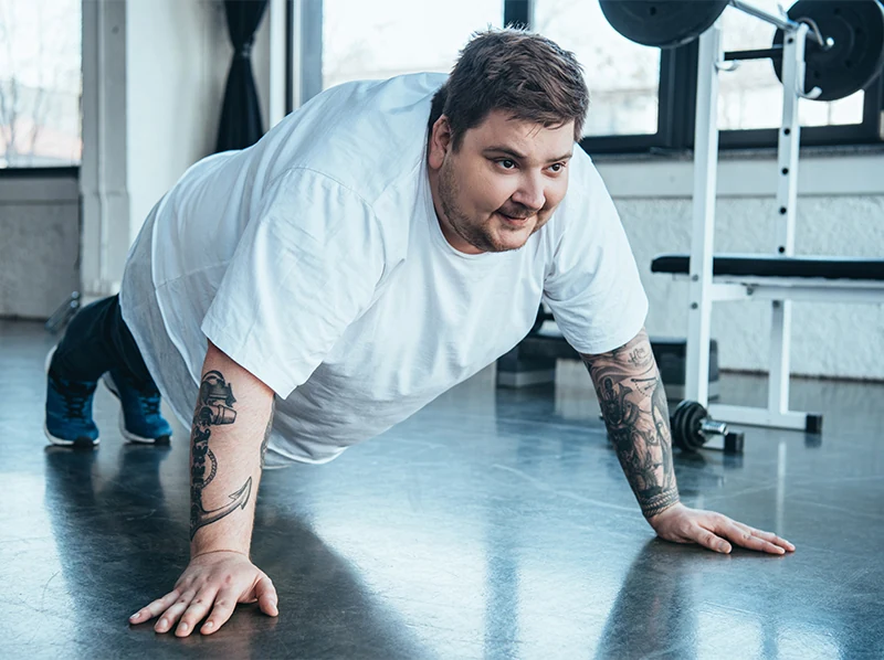 Overweight man doing pushups in gym