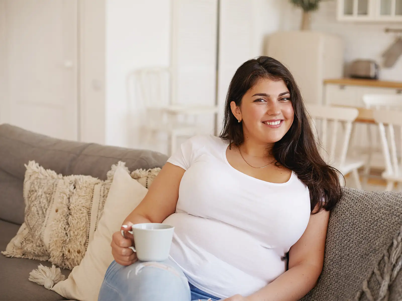 Plus size woman with coffee sitting on couch smiling