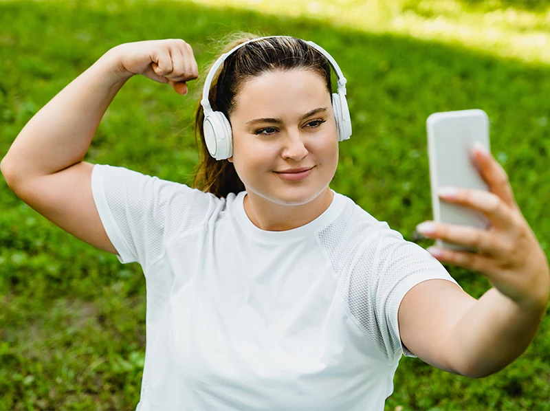 Confident plus size woman with headphones taking a selfie while flexing