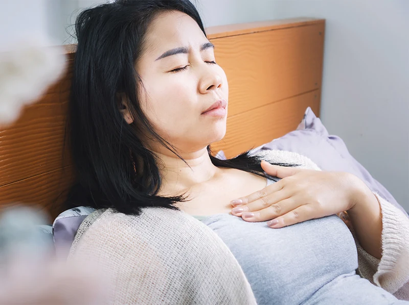 Woman with heartburn laying down in bed touching chest