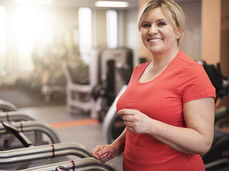 Smiling woman in pink shirt running on treadmill