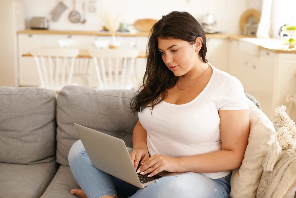 Woman sitting on her couch researching weight loss on the computer