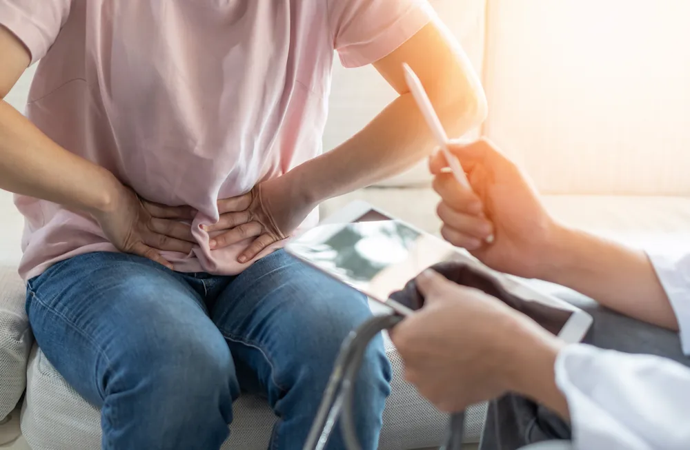 man holding his stomach in pain while discussing hernia options with a doctor