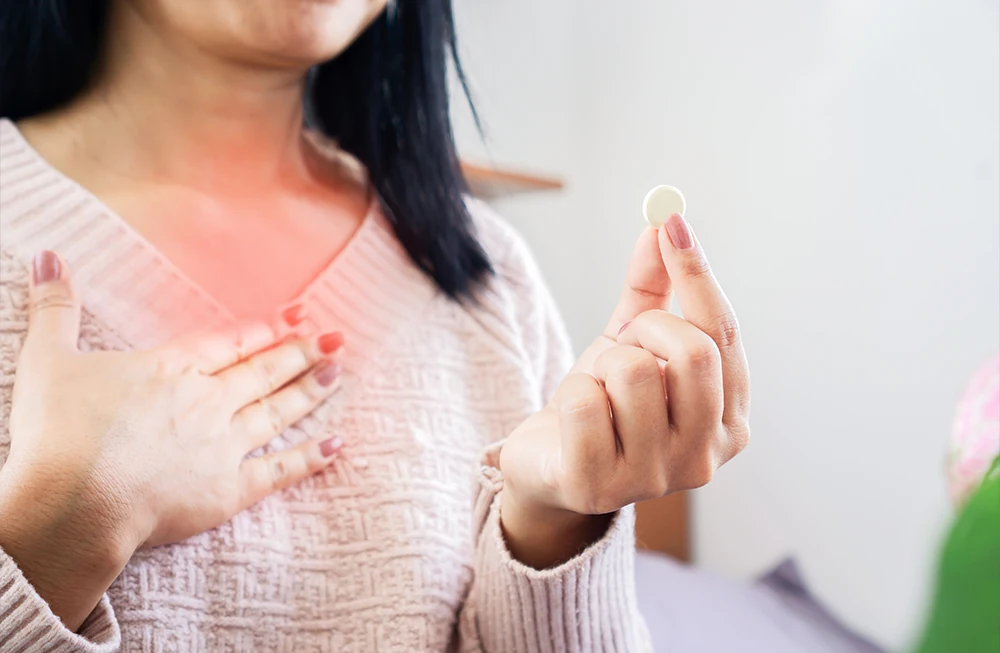 woman clutching chest in discomfort, still experiencing heartburn while holding acid reflux medication