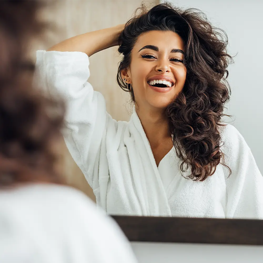 woman smiling in the mirror while holding her hair
